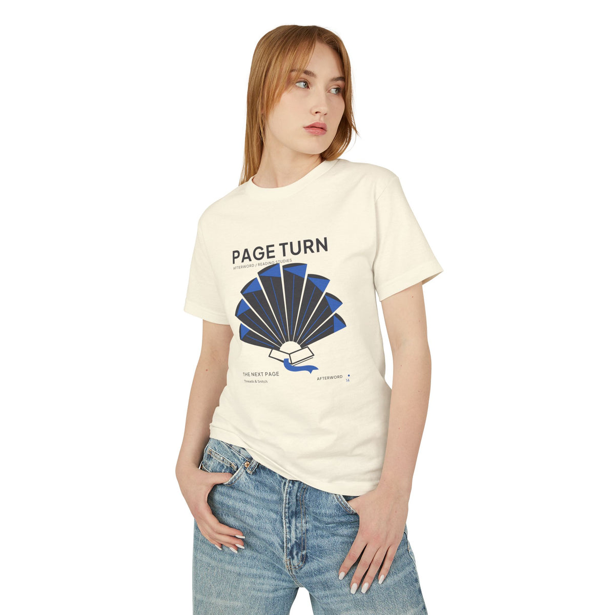 Model mockup of Page Turn Book Graphic Tee in Faded Cream, front view showing book pages fanned into a radial shape with blue folds and bookmark.