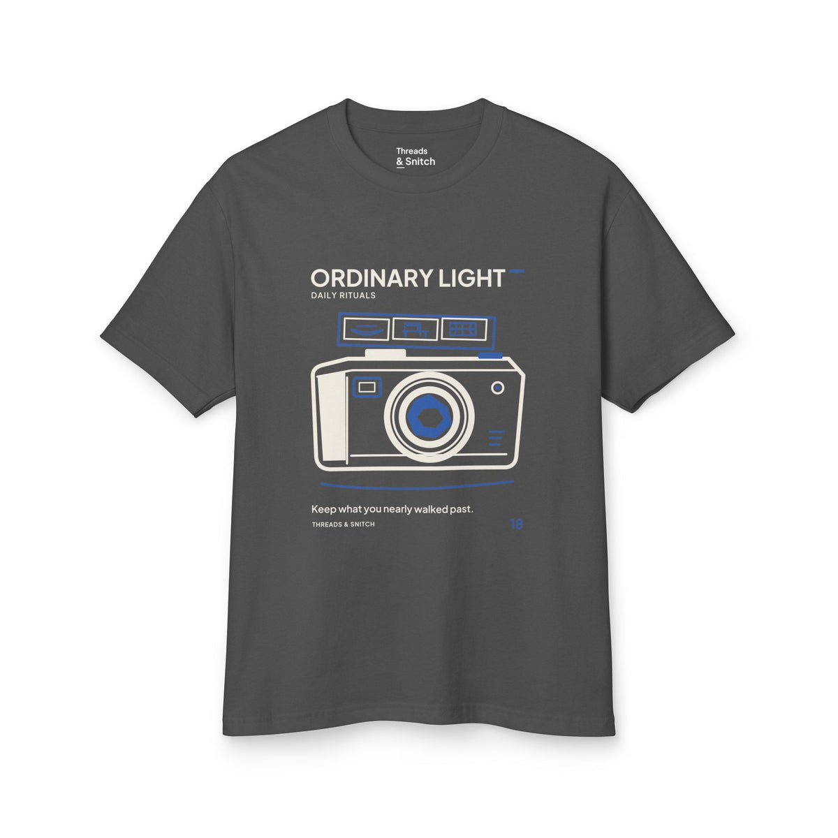 Mockup of Ordinary Light Camera Tee in Faded Black, front view showing camera with blue lens details and a strip of small domestic scenes.