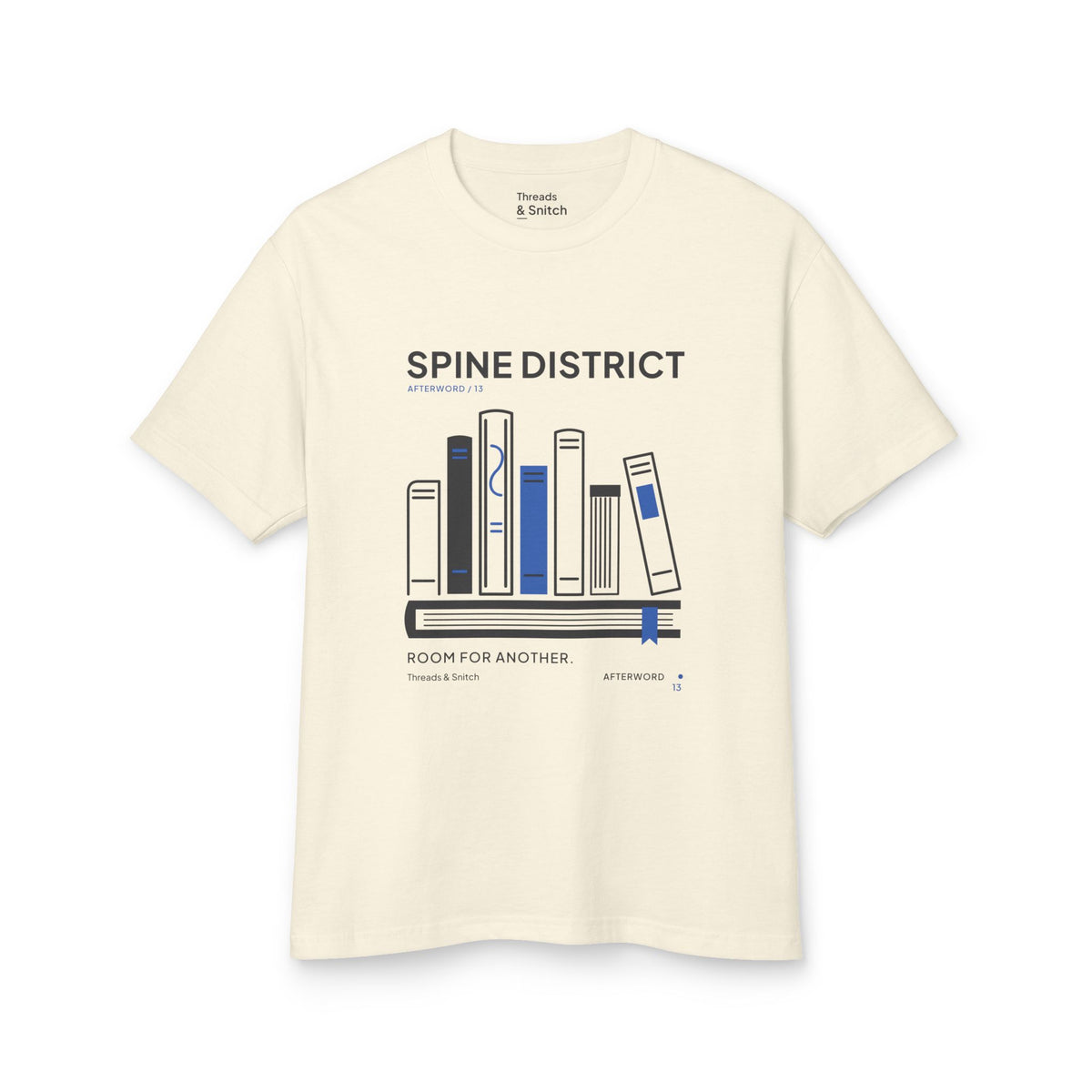 Mockup of Spine District Book Spine Tee in Faded Cream, front view showing varied book spines arranged as a skyline above a horizontal book.