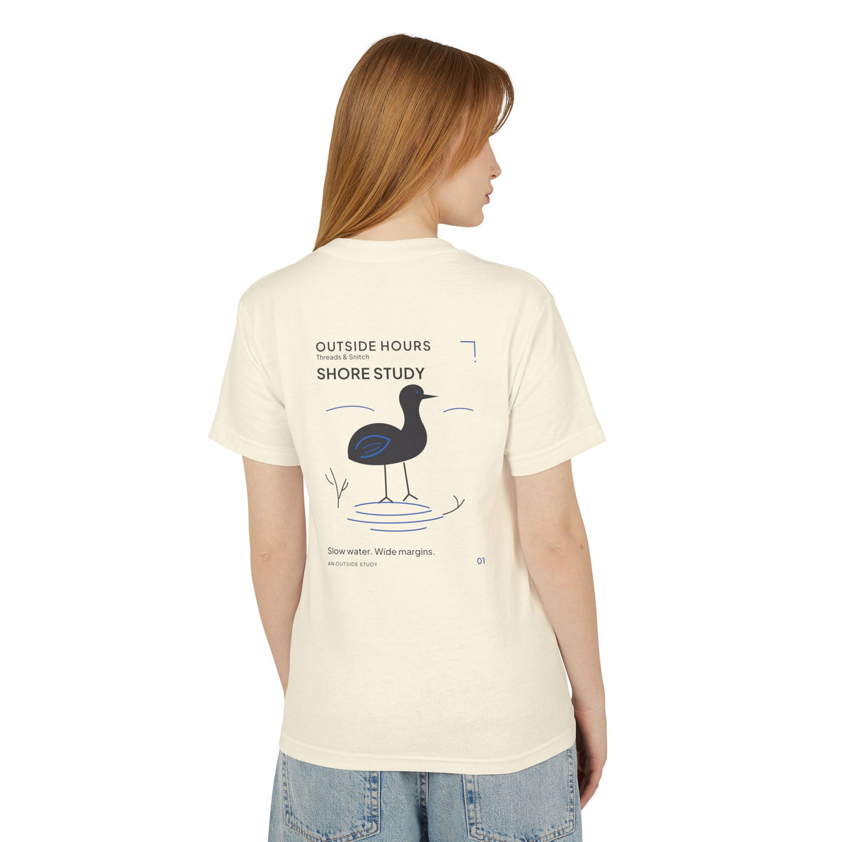 Back-view model mockup of Shore Study Bird Graphic Tee in Faded Cream, showing the wading bird and shoreline illustration.