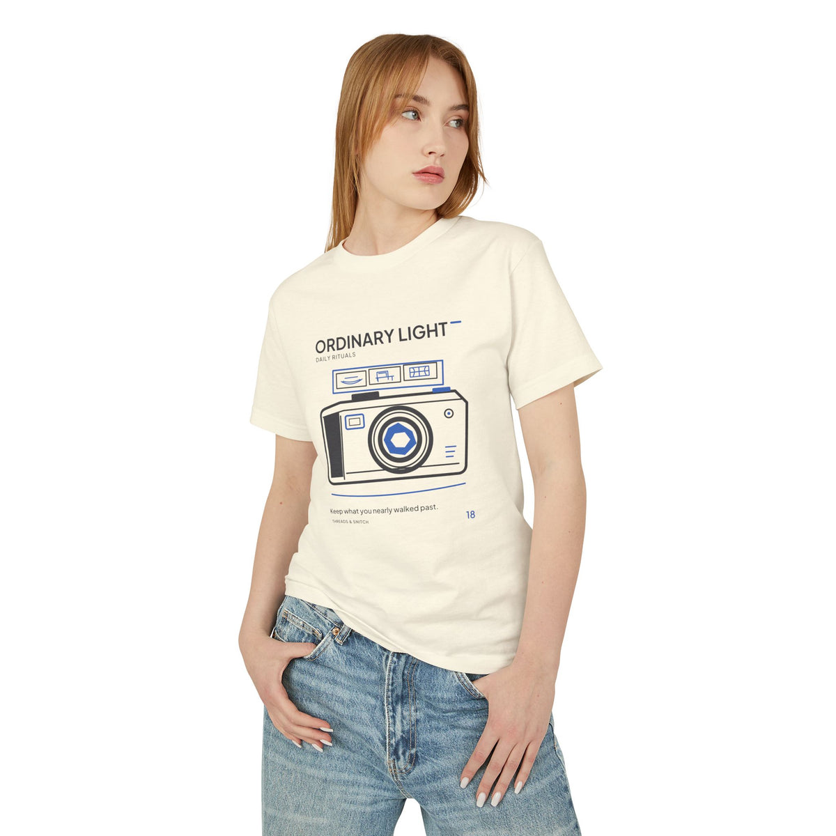 Model mockup of Ordinary Light Camera Tee in Faded Cream, front view showing camera with blue lens details and a strip of small domestic scenes.