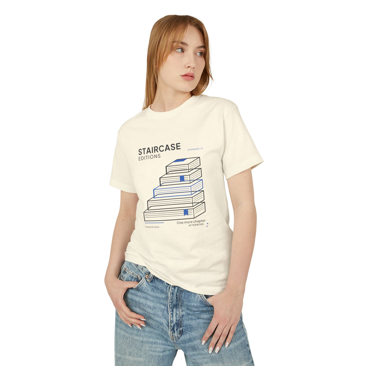 Model mockup of Staircase Editions Book Stack Tee in Faded Cream, front view showing five staggered books forming stairs with blue bookmarks.