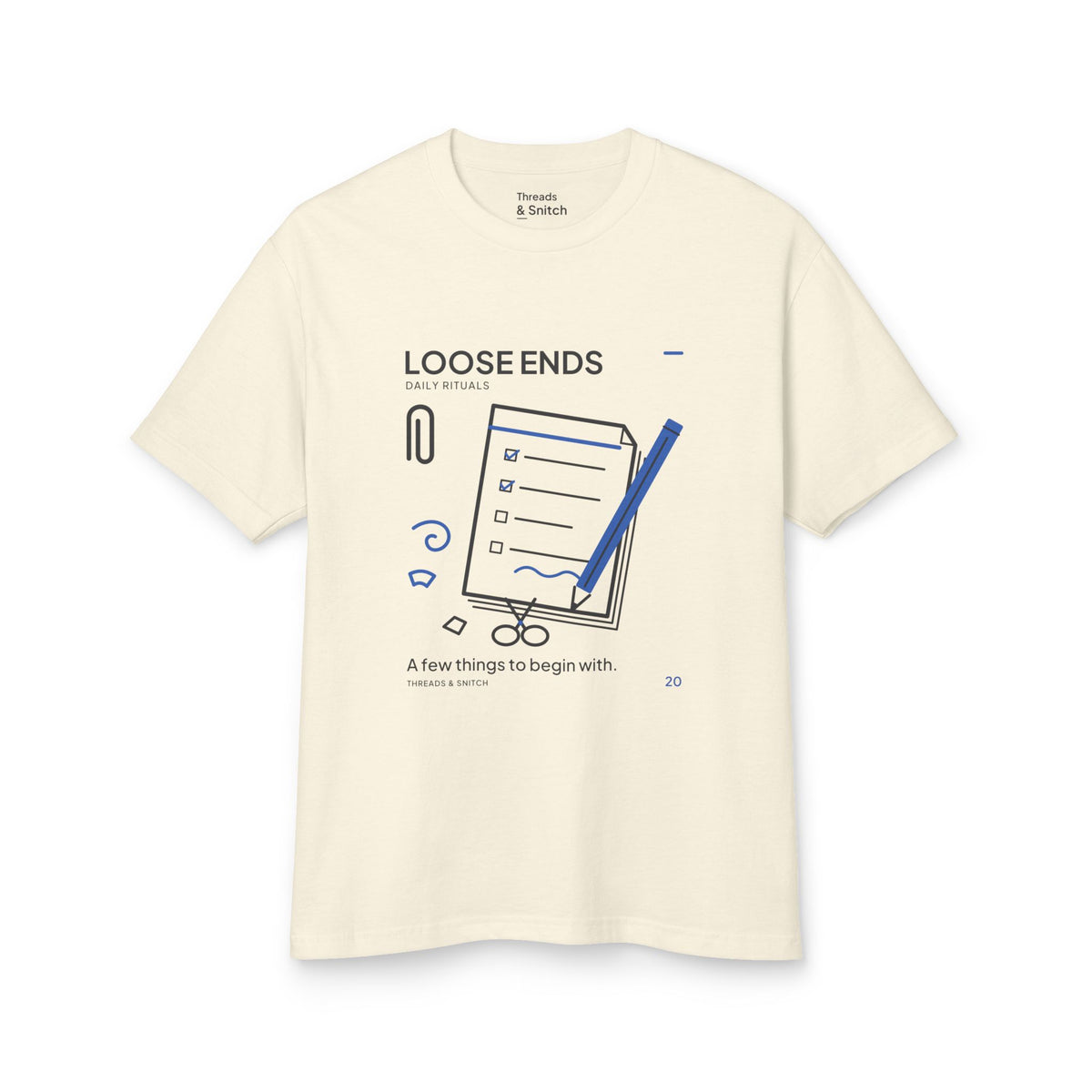 Mockup of Loose Ends Stationery Tee in Faded Cream, front view showing diagonal pencil over a task pad with scissors and a paper clip.