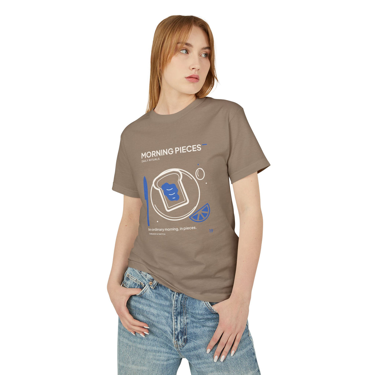 Model mockup of Morning Pieces Breakfast Tee in Faded Brown, front view showing toast on a plate beside a citrus slice and blue knife.