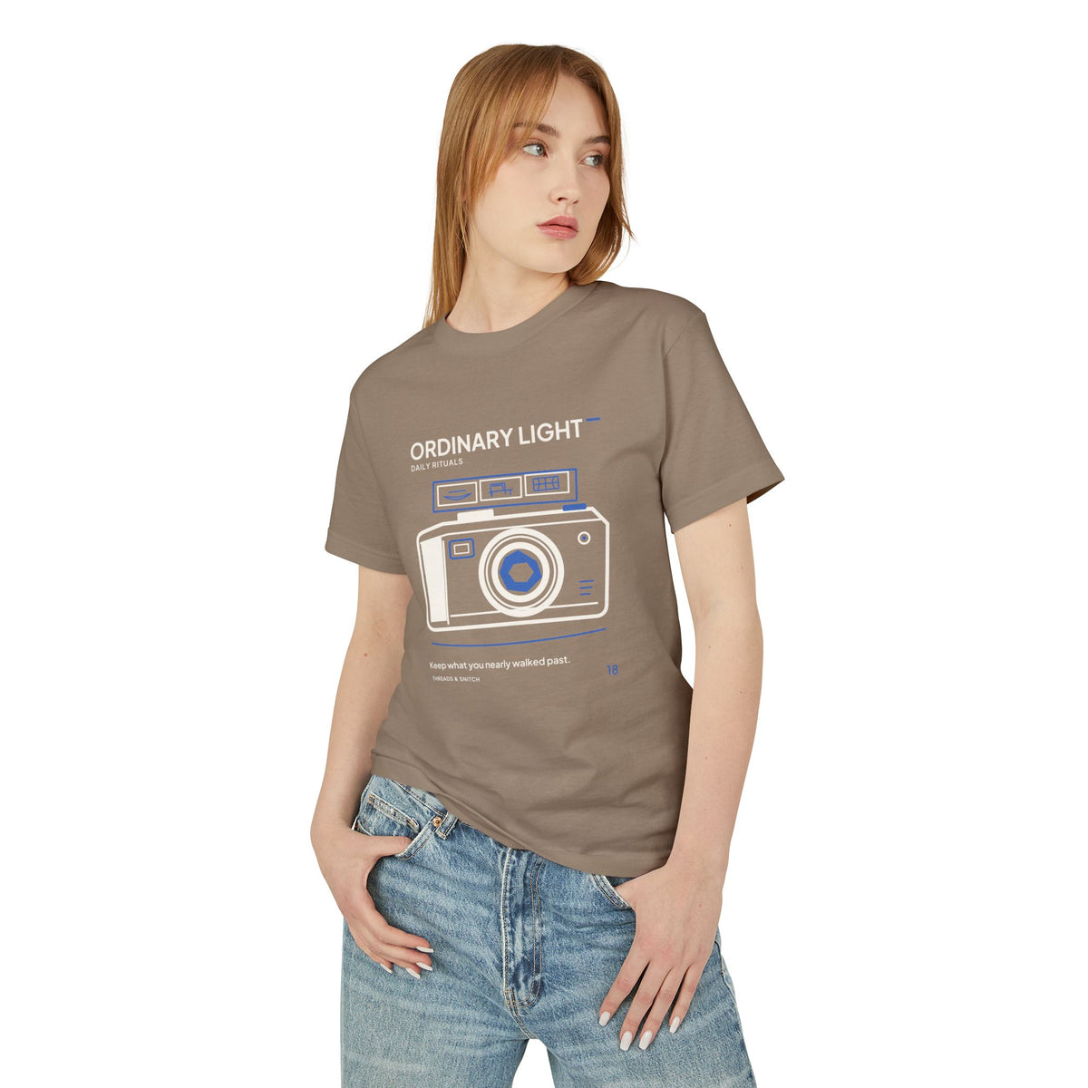 Model mockup of Ordinary Light Camera Tee in Faded Brown, front view showing camera with blue lens details and a strip of small domestic scenes.