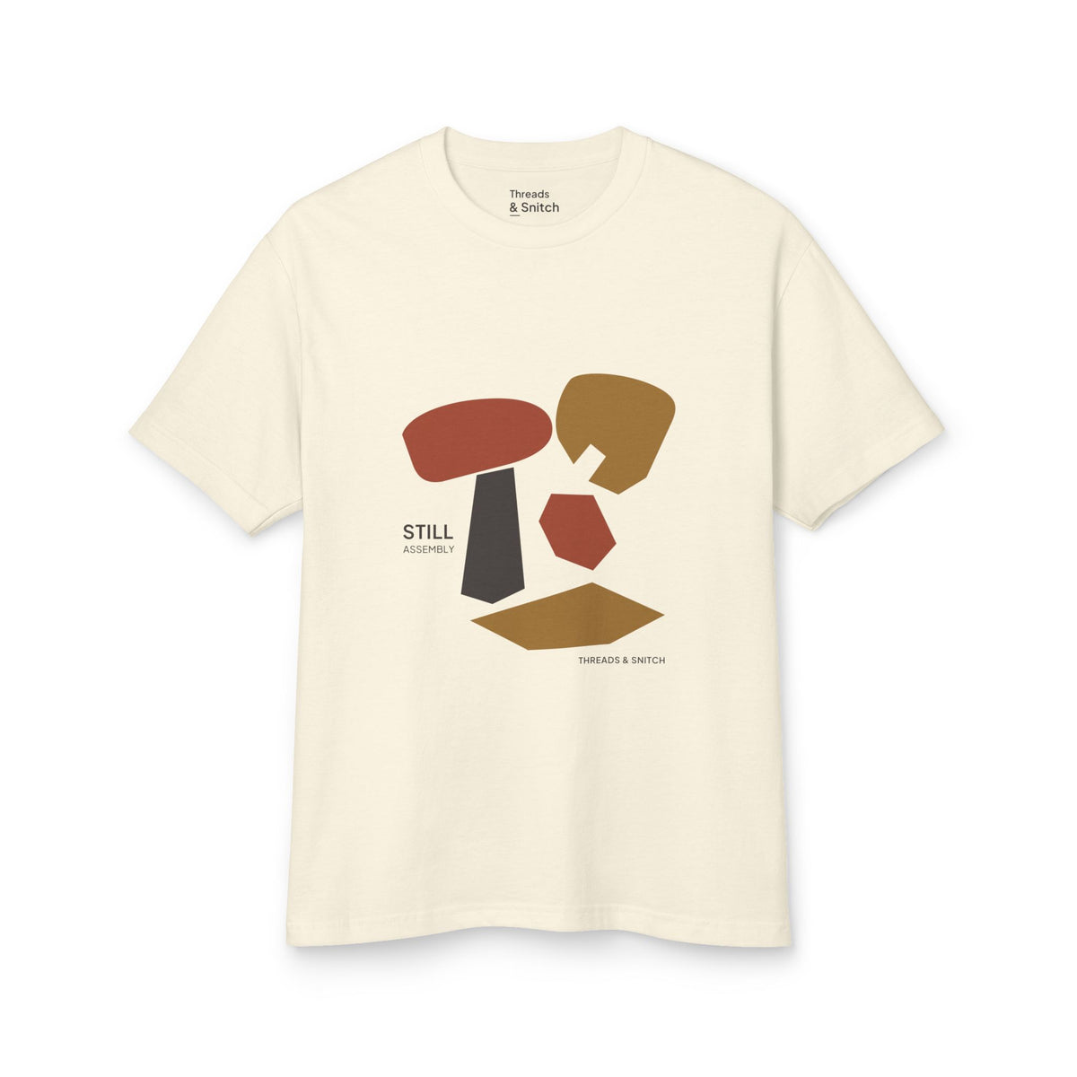 Mockup of Still Assembly Abstract Graphic Tee in Faded Cream, front view showing floating rounded and angular sculptural forms with Still Assembly lettering.