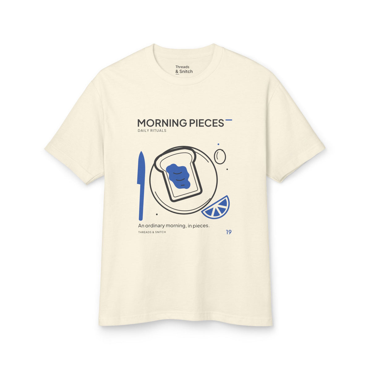 Mockup of Morning Pieces Breakfast Tee in Faded Cream, front view showing toast on a plate beside a citrus slice and blue knife.