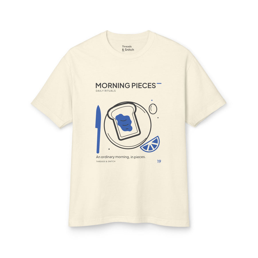 Mockup of Morning Pieces Breakfast Tee in Faded Cream, front view showing toast on a plate beside a citrus slice and blue knife.