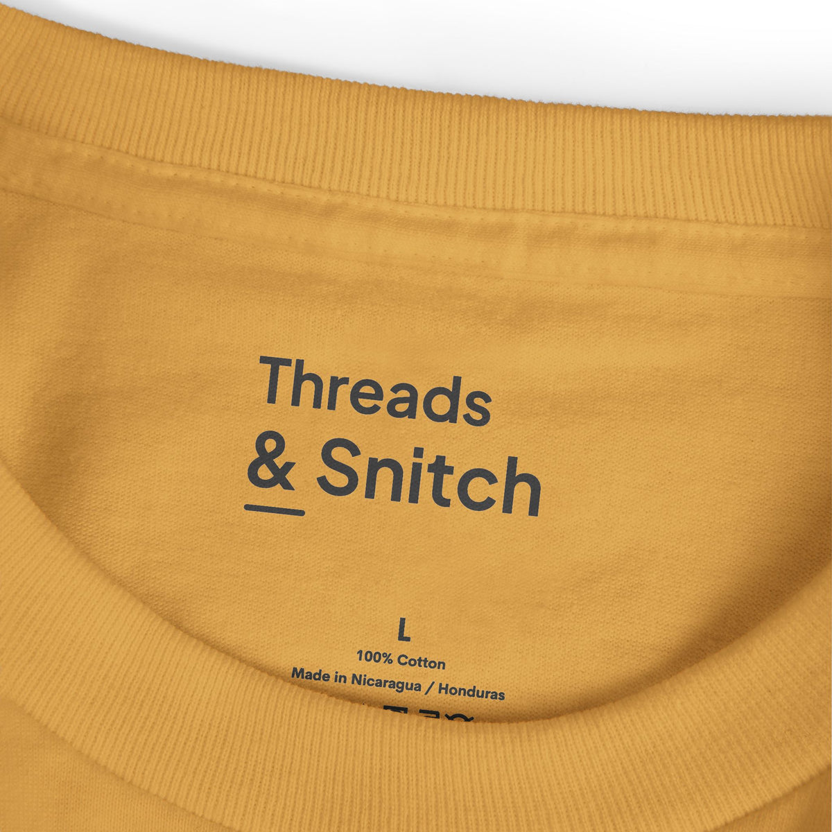 Mockup detail of the printed Threads & Snitch inner-neck label on Morning Pieces Breakfast Tee in Faded Mustard.