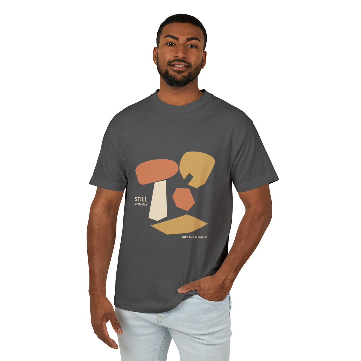 Model mockup of Still Assembly Abstract Graphic Tee in Faded Black, front view showing floating rounded and angular sculptural forms with Still Assembly lettering.