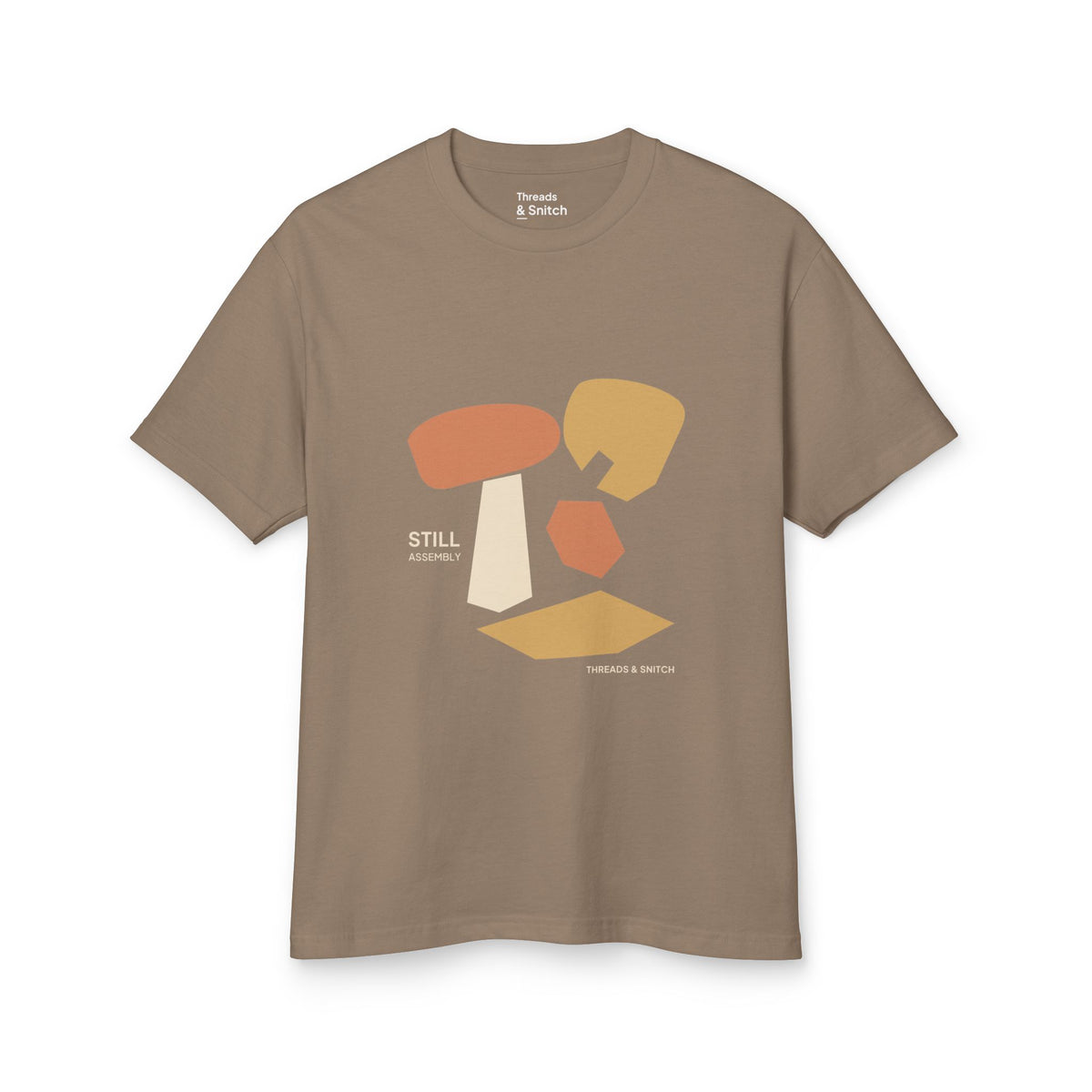 Mockup of Still Assembly Abstract Graphic Tee in Faded Brown, front view showing floating rounded and angular sculptural forms with Still Assembly lettering.