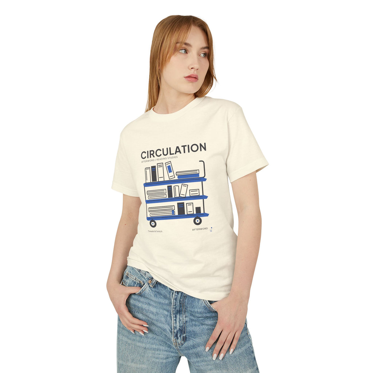 Model mockup of Circulation Library Cart Tee in Faded Cream, front view showing three-tier library cart filled with books and blue shelves.