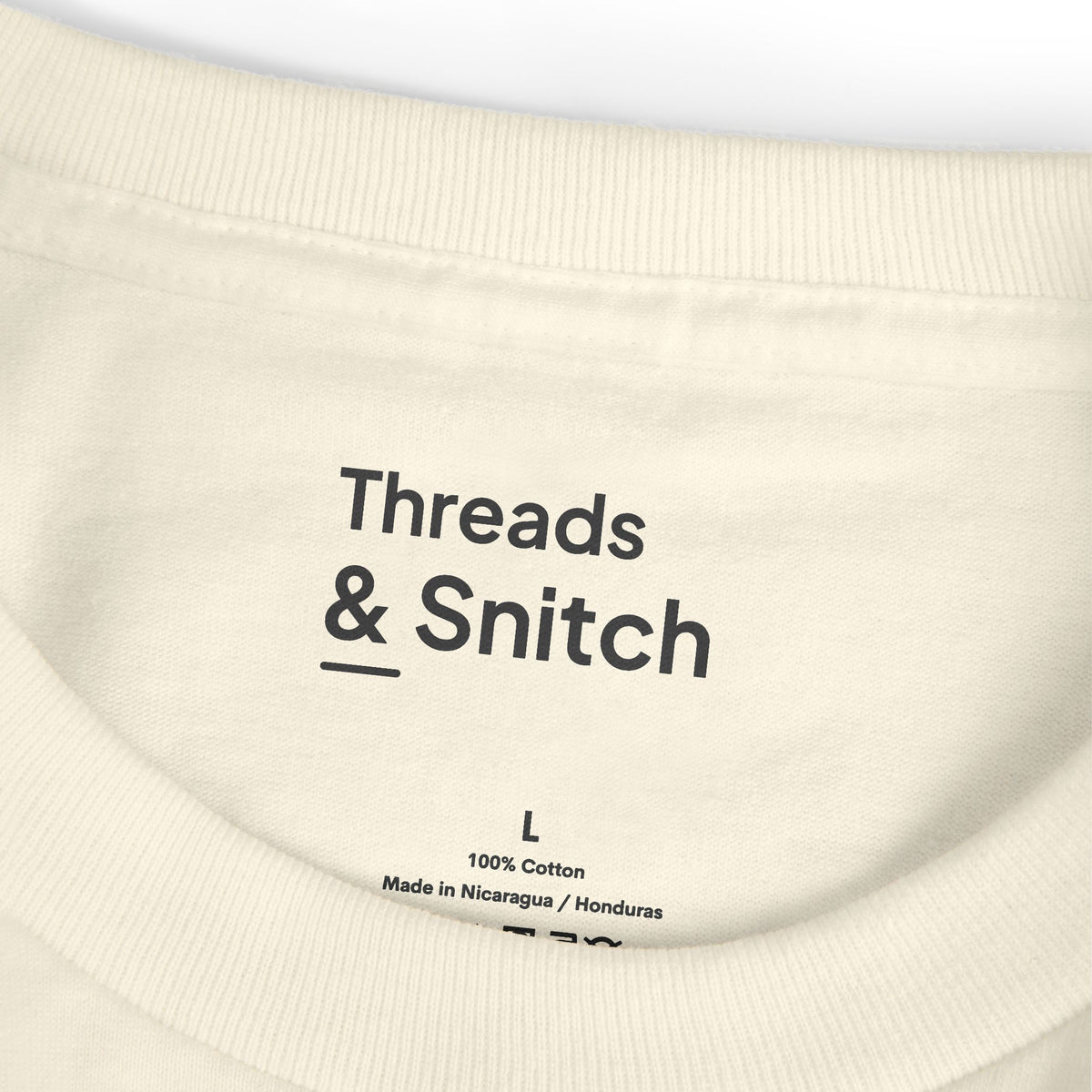 Mockup detail of the printed Threads & Snitch inner-neck label on Morning Pieces Breakfast Tee in Faded Cream.