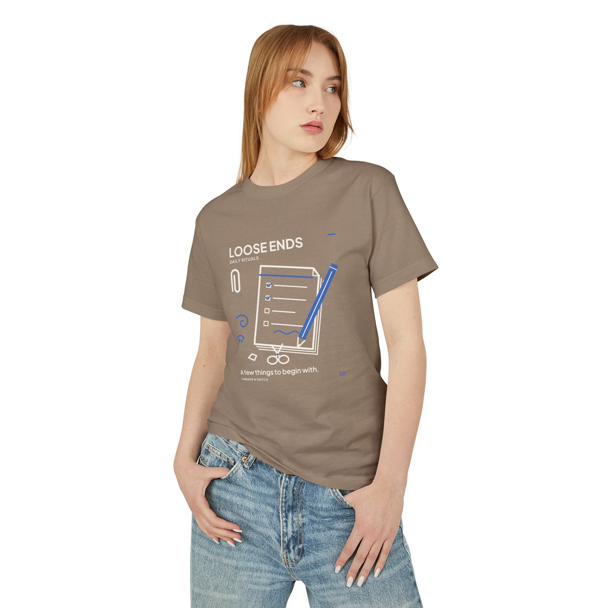 Model mockup of Loose Ends Stationery Tee in Faded Brown, front view showing diagonal pencil over a task pad with scissors and a paper clip.