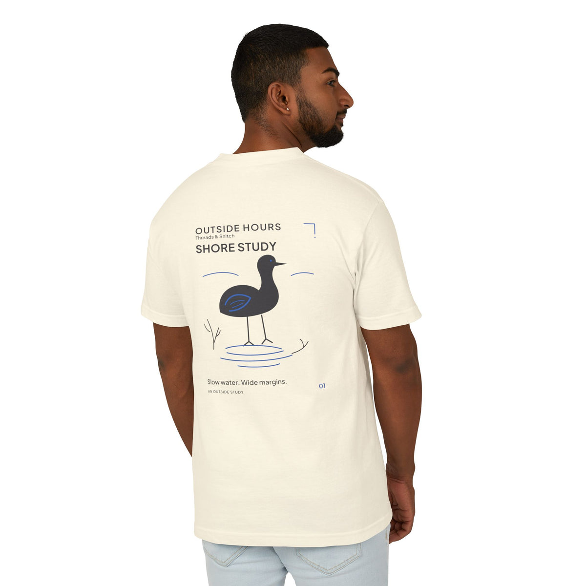 Back-view model mockup of Shore Study Bird Graphic Tee in Faded Cream, showing the wading bird and shoreline illustration.