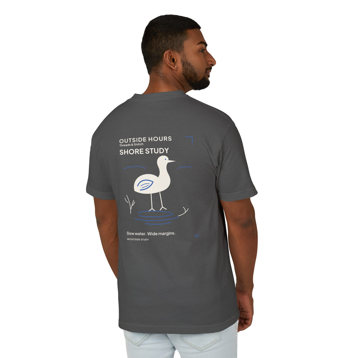 Back-view model mockup of Shore Study Bird Graphic Tee in Faded Black, showing the wading bird and shoreline illustration.
