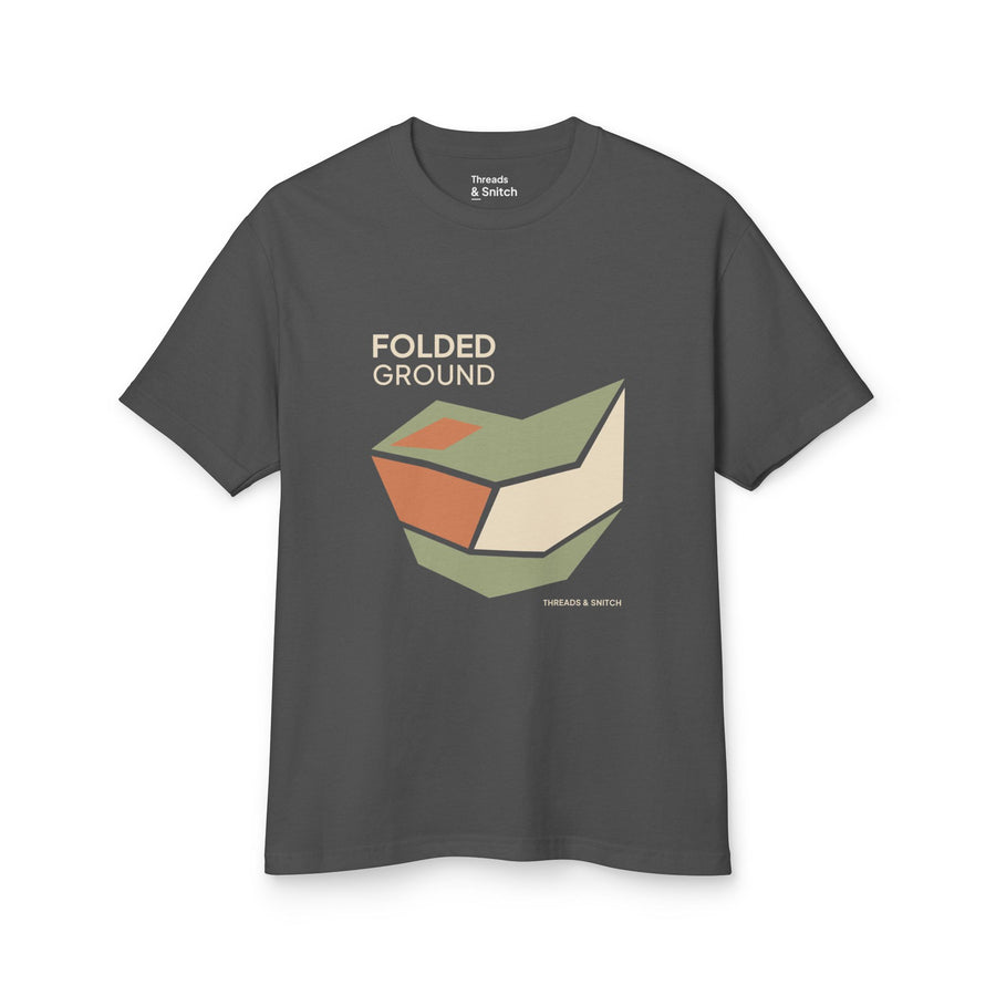 Mockup of Folded Ground Geometric Graphic Tee in Faded Black, front view showing angular folded planes with open channels and Folded Ground lettering.