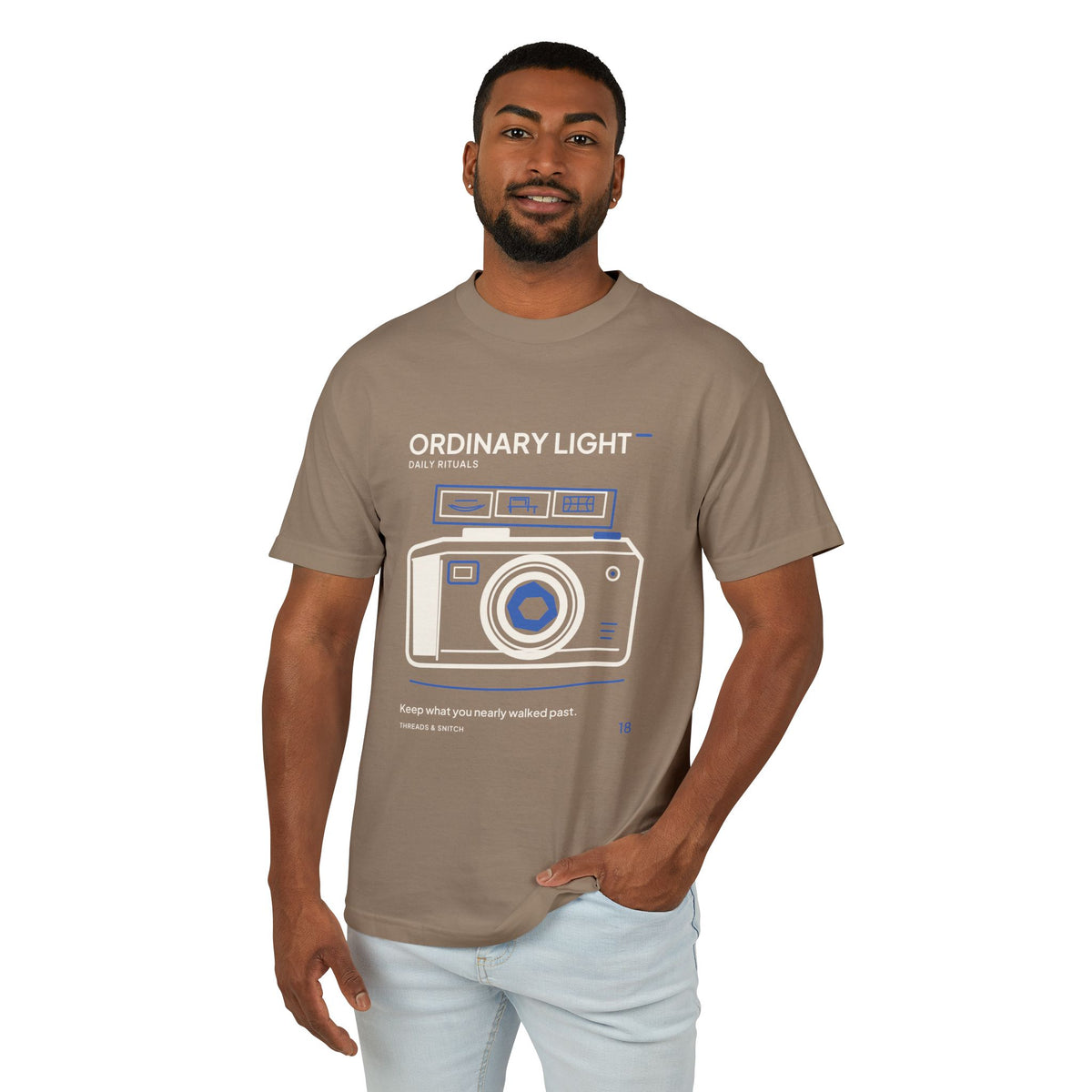 Model mockup of Ordinary Light Camera Tee in Faded Brown, front view showing camera with blue lens details and a strip of small domestic scenes.