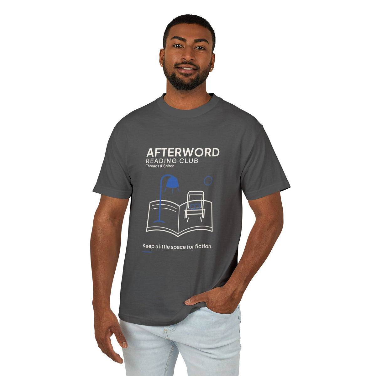 Model mockup of Afterword Reading Room Tee in Faded Black, front view showing open book forming a room with an armchair and blue lamp.