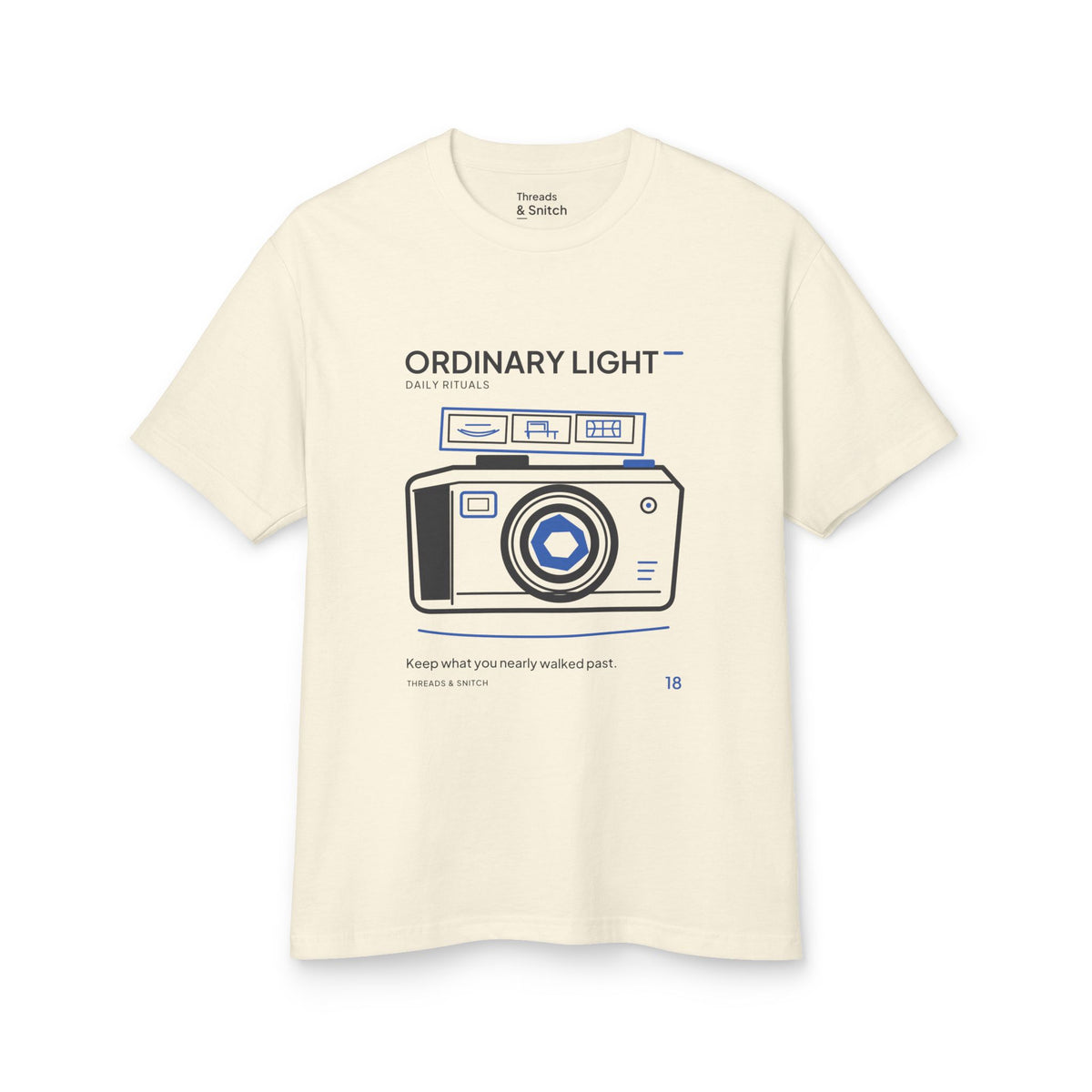 Mockup of Ordinary Light Camera Tee in Faded Cream, front view showing camera with blue lens details and a strip of small domestic scenes.