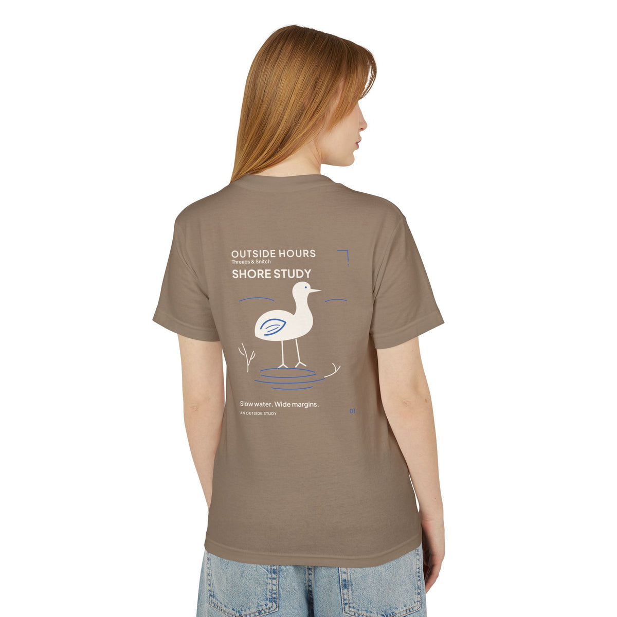 Back-view model mockup of Shore Study Bird Graphic Tee in Faded Brown, showing the wading bird and shoreline illustration.