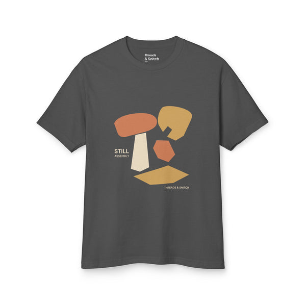 Mockup of Still Assembly Abstract Graphic Tee in Faded Black, front view showing floating rounded and angular sculptural forms with Still Assembly lettering.