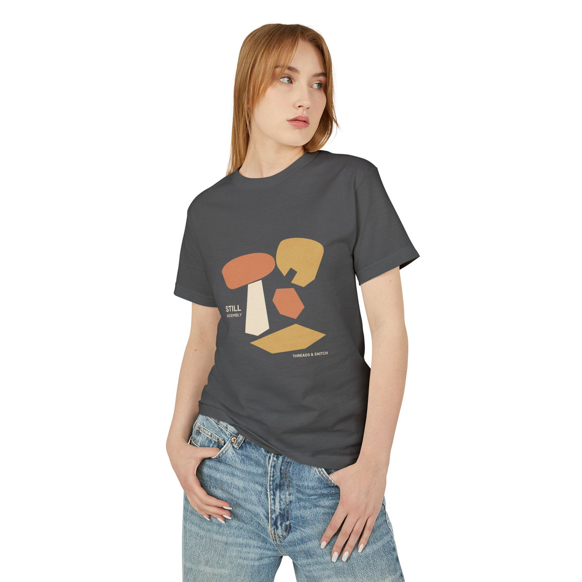 Model mockup of Still Assembly Abstract Graphic Tee in Faded Black, front view showing floating rounded and angular sculptural forms with Still Assembly lettering.