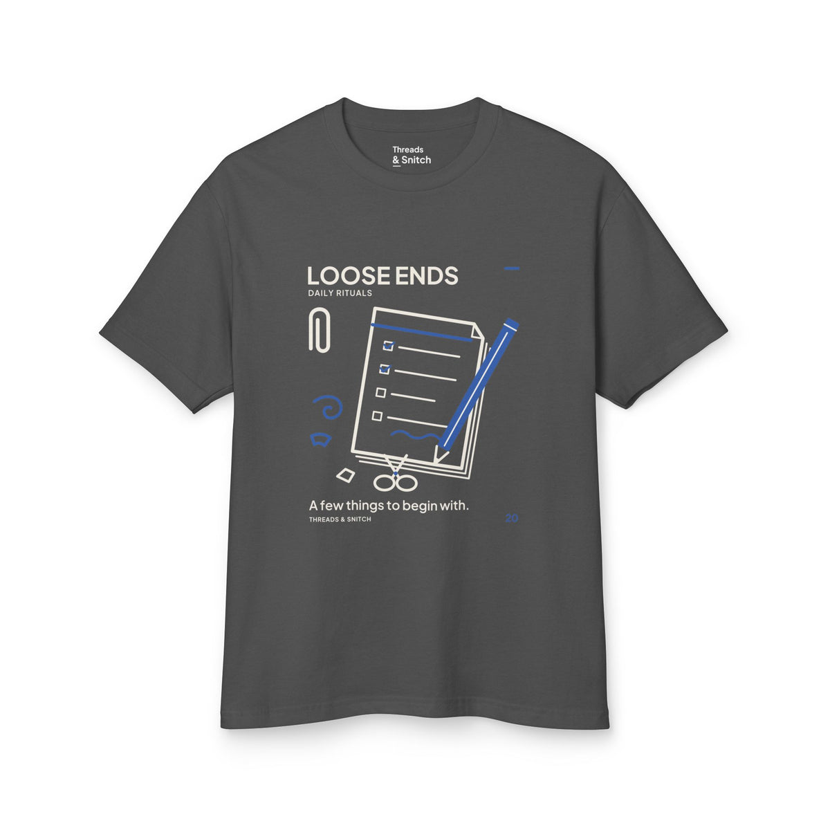 Mockup of Loose Ends Stationery Tee in Faded Black, front view showing diagonal pencil over a task pad with scissors and a paper clip.