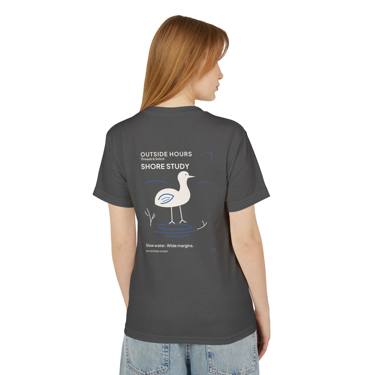 Back-view model mockup of Shore Study Bird Graphic Tee in Faded Black, showing the wading bird and shoreline illustration.