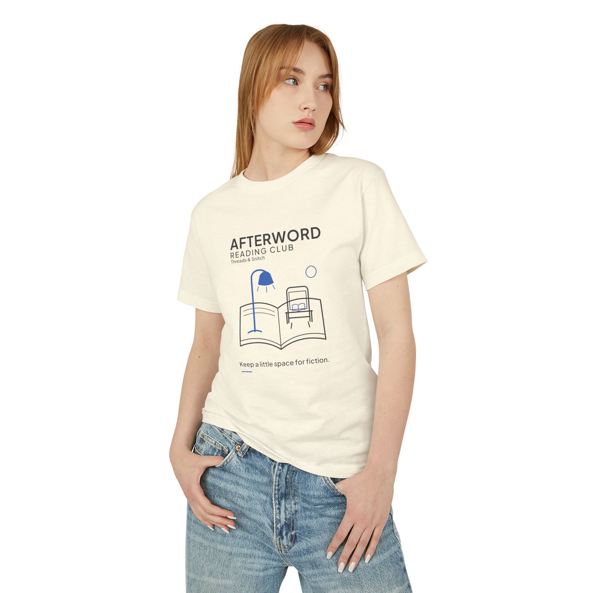 Model mockup of Afterword Reading Room Tee in Faded Cream, front view showing open book forming a room with an armchair and blue lamp.