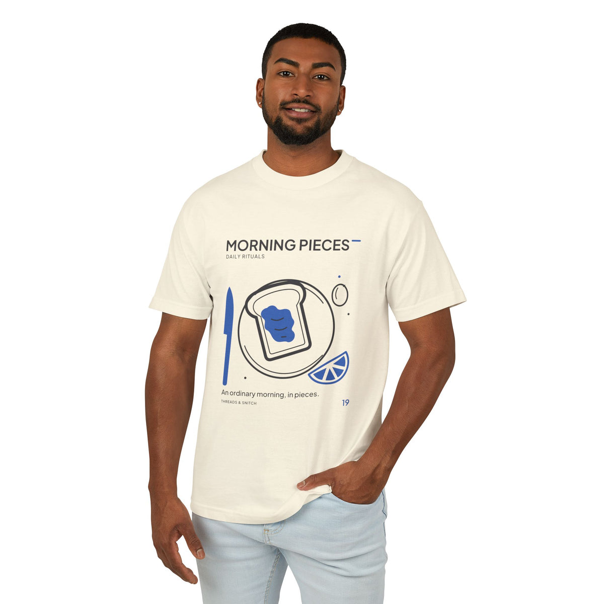 Model mockup of Morning Pieces Breakfast Tee in Faded Cream, front view showing toast on a plate beside a citrus slice and blue knife.